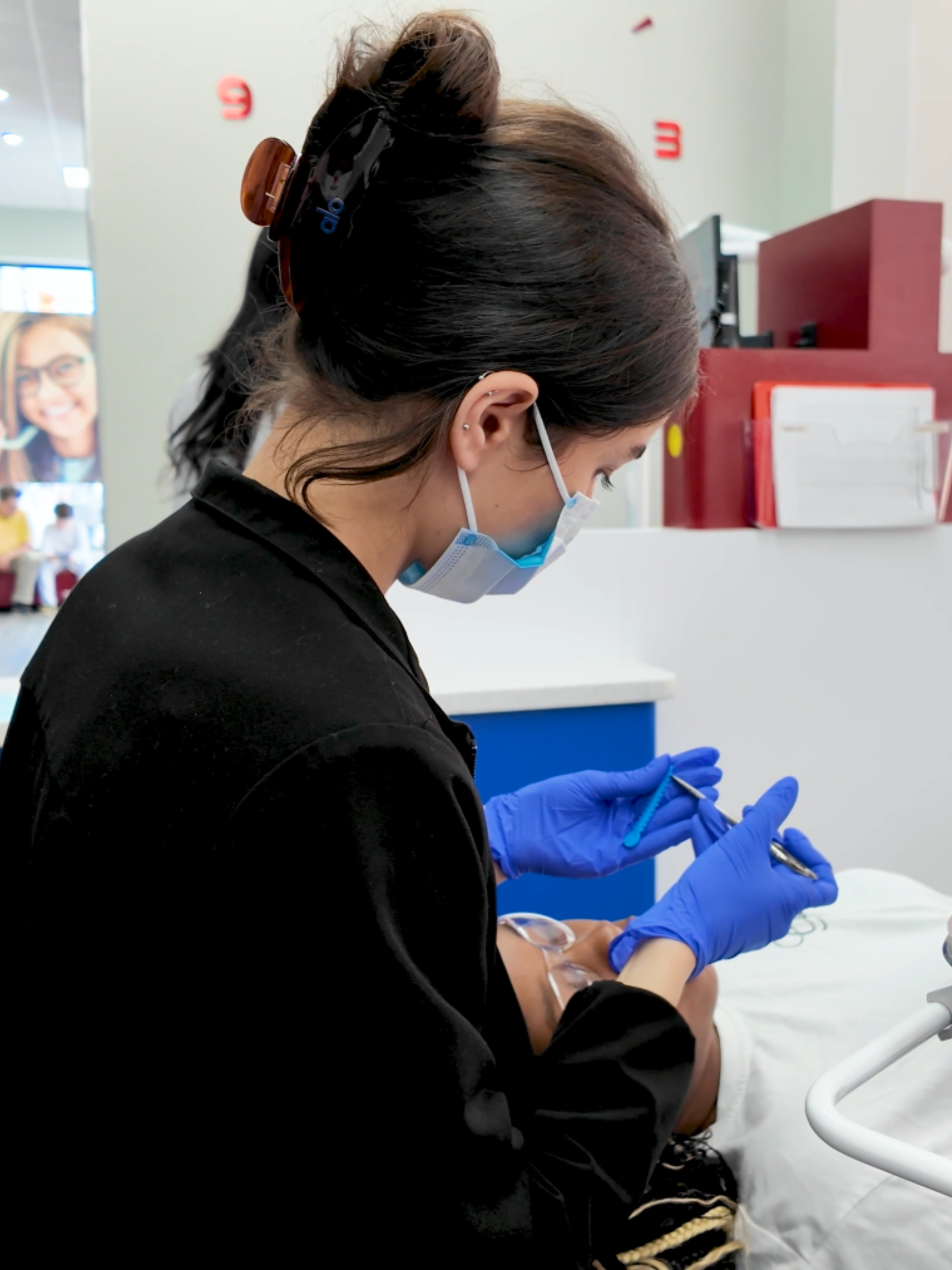 Orthodontist in a medical setting wearing gloves and a mask, attending to a traditional braces' patient.
