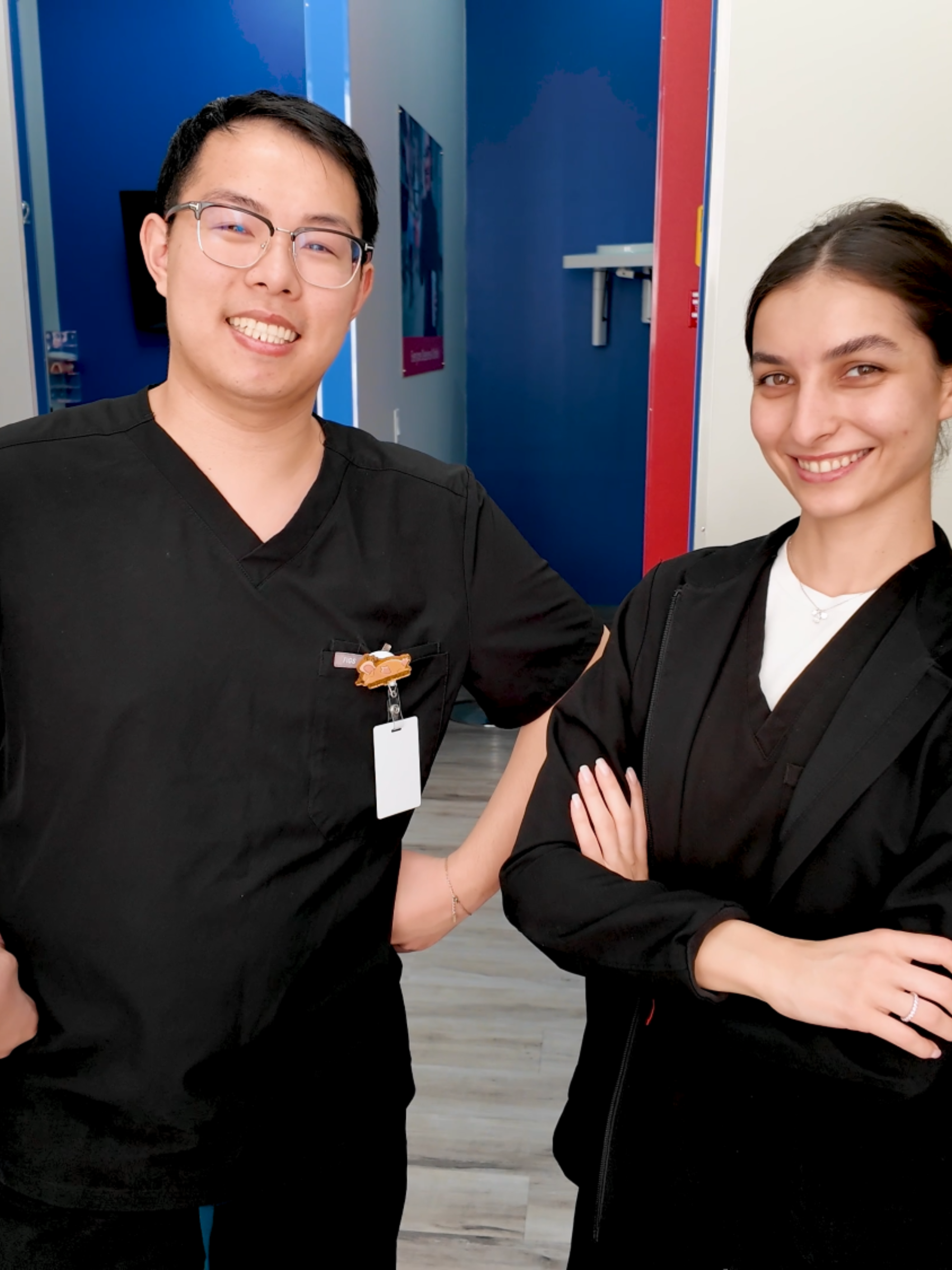 An orthodontist a dental hygienist in black uniforms standing in a room with blue walls.