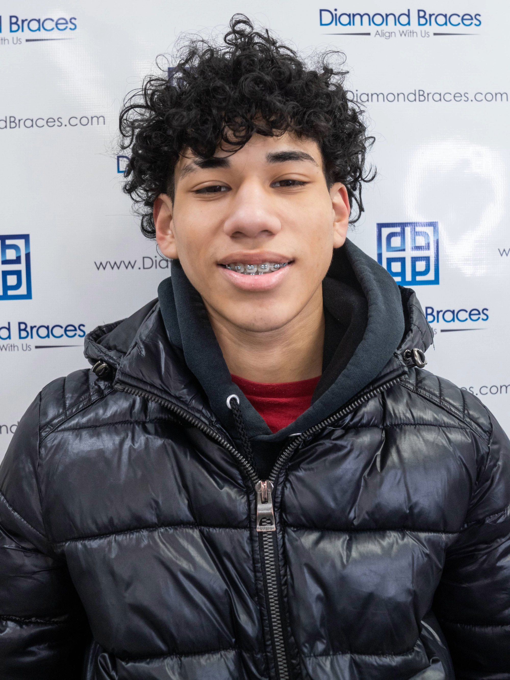 Dental care patient wearing a black puffer jacket in front of a Diamond Braces promotional backdrop.