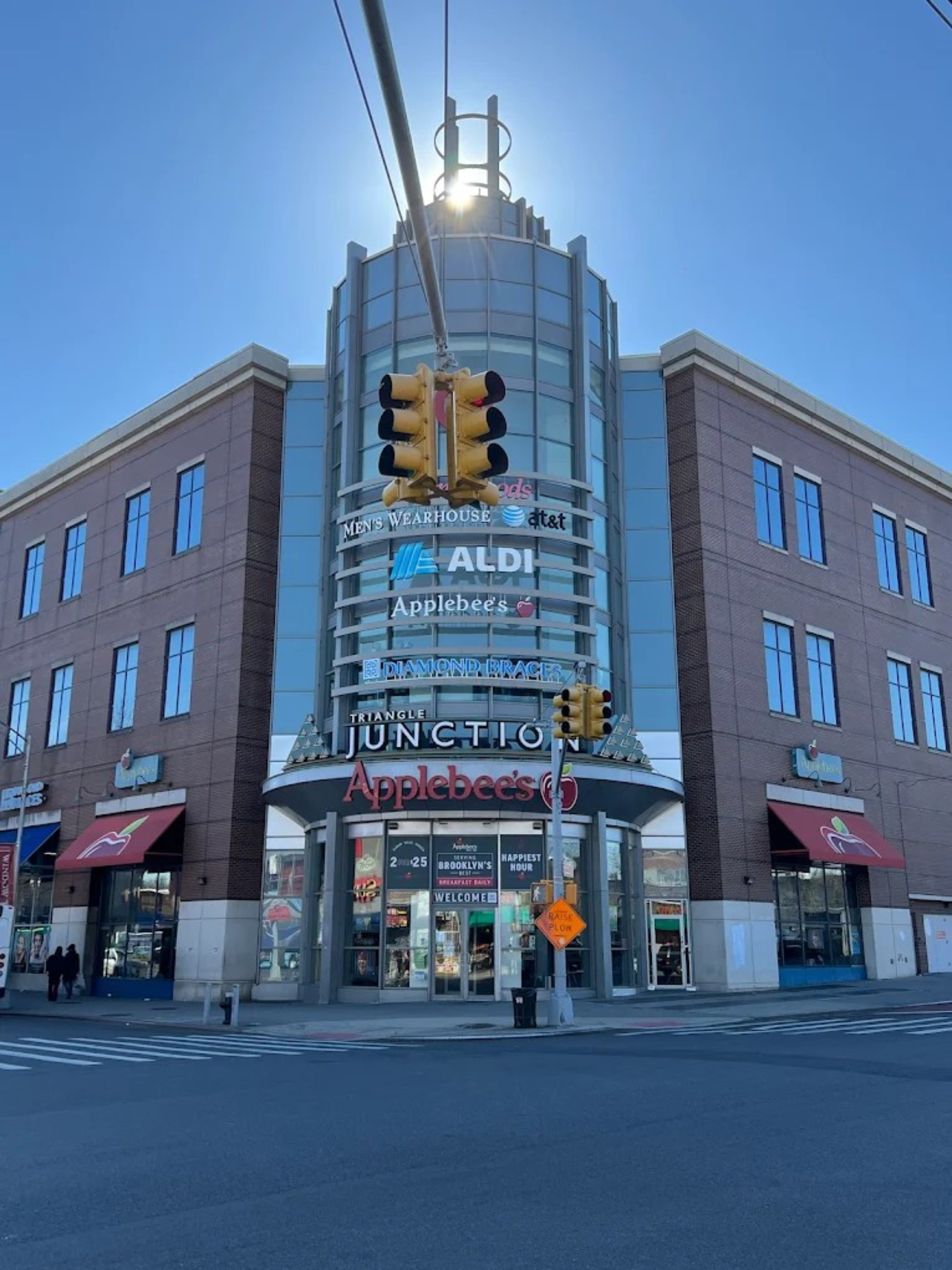 Commercial building with multiple store signs including Aldi and Applebee's, under a clear blue sky.