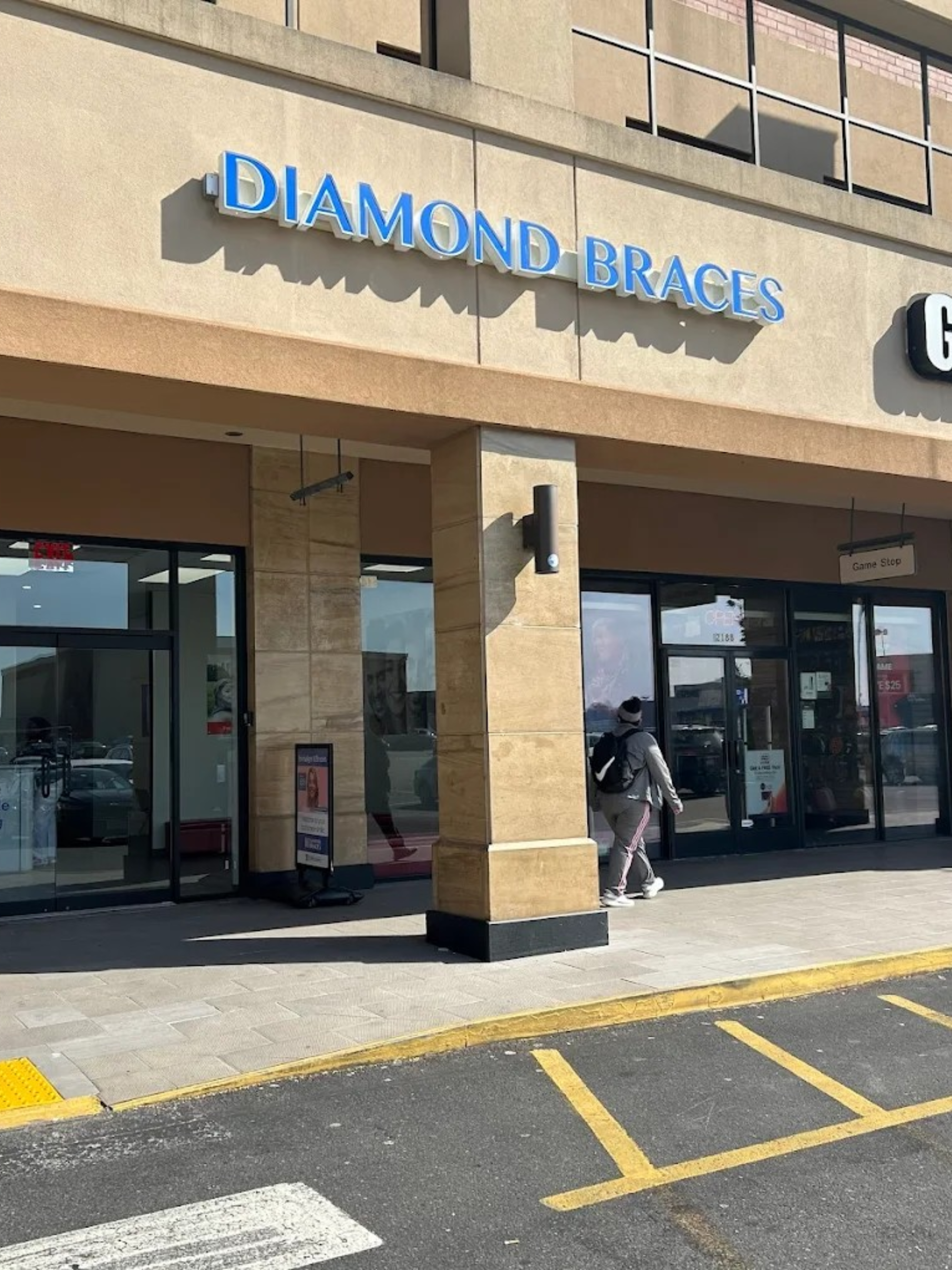 Diamond Braces orthodontist office store front with a person walking by in Bay Plaza, New York.