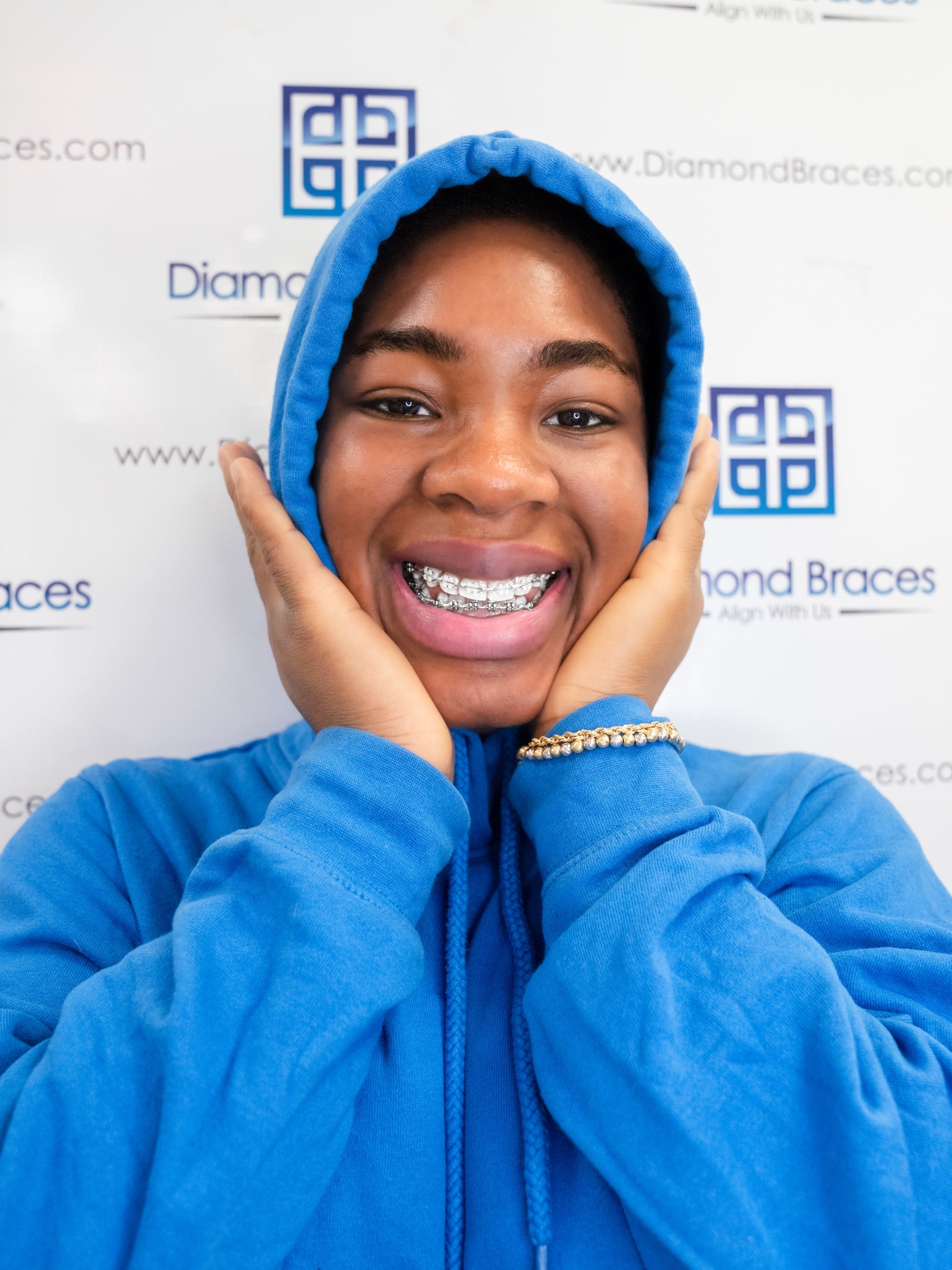 Dental care patient wearing a blue hoodie with a Diamond Braces logo in the background.