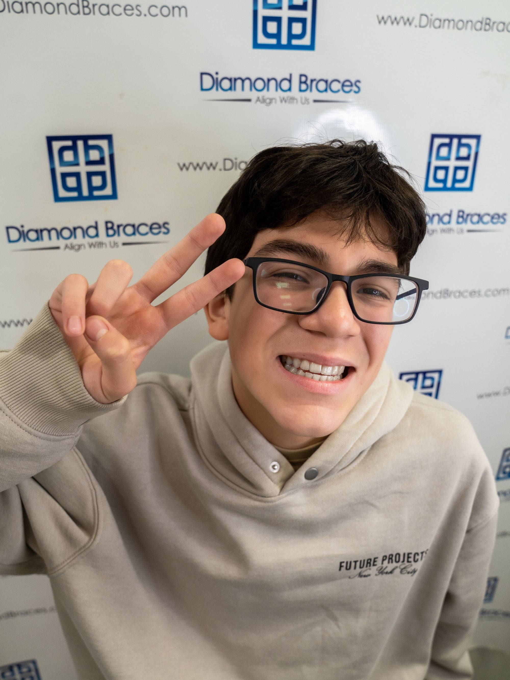 Dental care patient making a peace sign in front of a Diamond Braces backdrop.