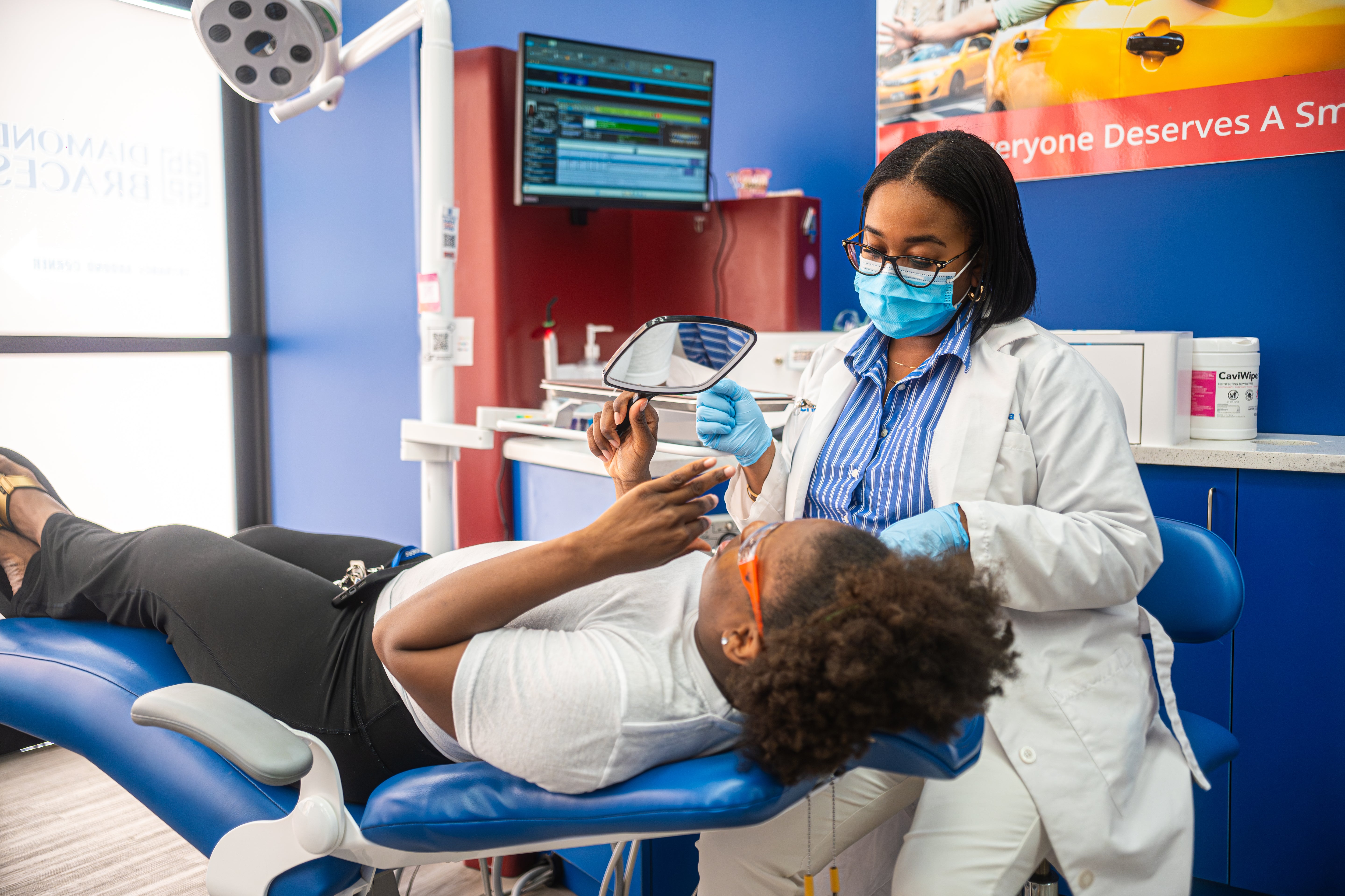 Dental hygienist examining a patient in a Diamond Braces dental office with dental equipment and a 'Smile' sign in the background.
