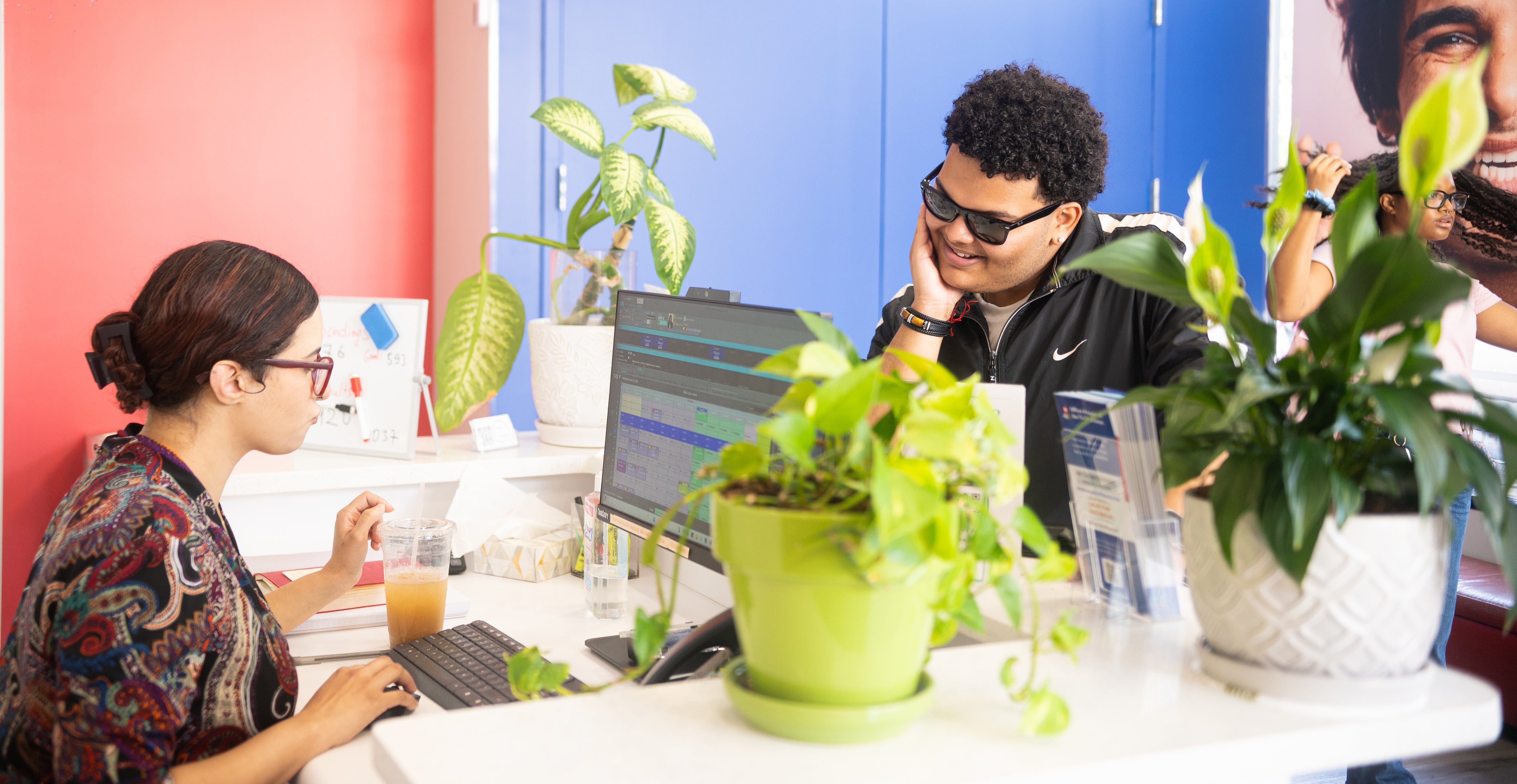 Two people working at a desk with plants and colorful walls