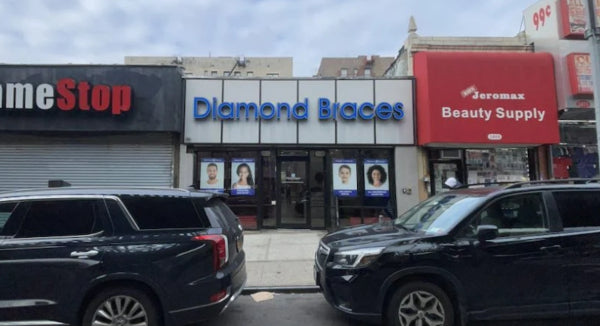 Commercial street scene with 'Diamond Braces' and 'Jeremax Beauty Supply' stores, cars parked in front on a main street in Brooklyn.