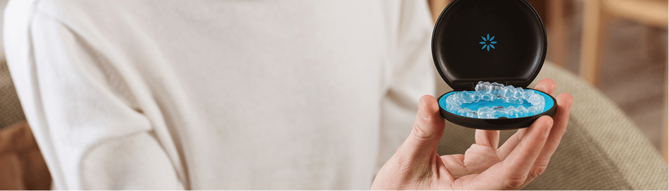 Person holding a small round container with a lid open, revealing a blue object inside.