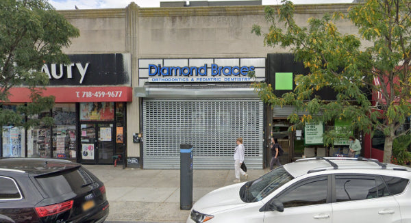 Commercial street scene in Rego Park with a Diamond Braces dentist office and 'beauty' signs, cars parked on the street.