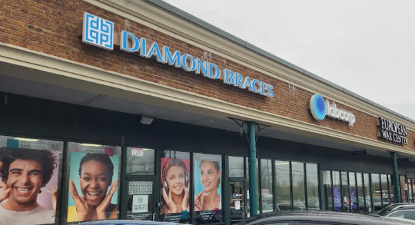 Diamond Braces dental care office exterior with multiple signs and images on the window in a Long Island strip mall.