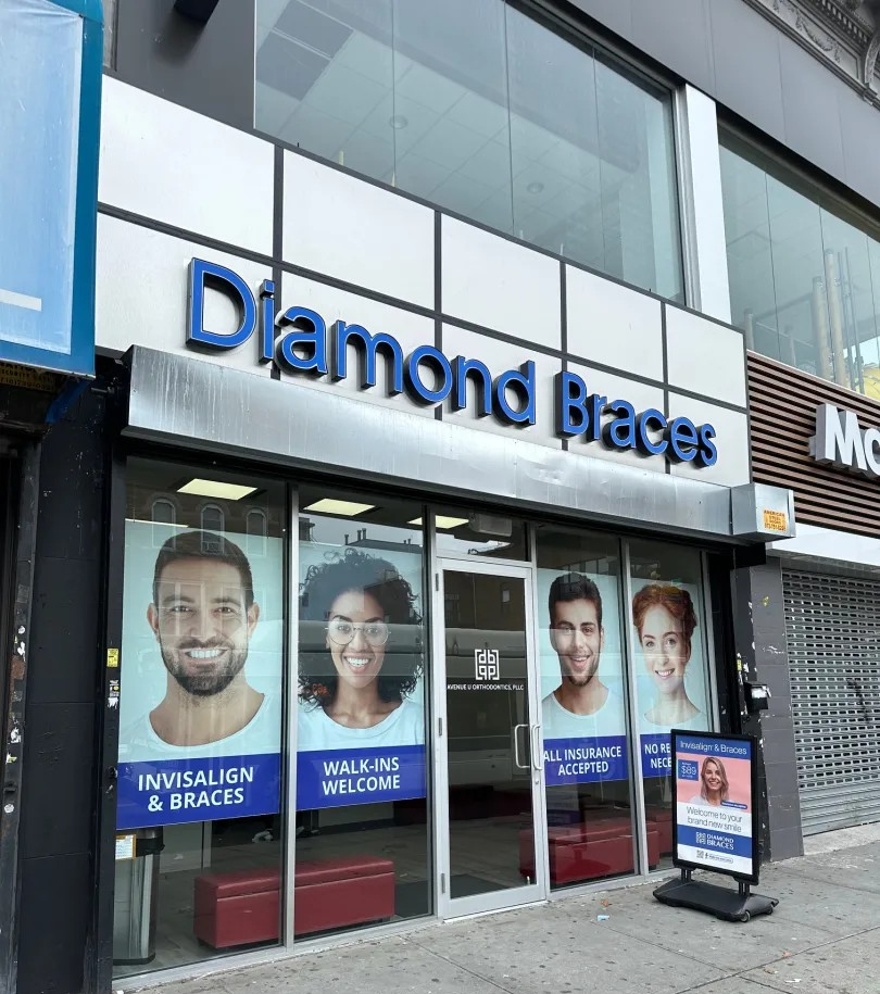 Diamond Braces dental care clinic exterior with promotional posters on a glass facade in Sunset Park, Brooklyn.