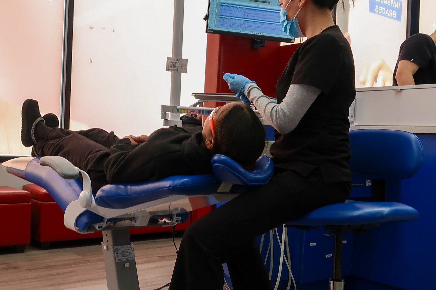 Low angle photo of an orthodontist sitting down over her patient who is getting braces for kids. 
