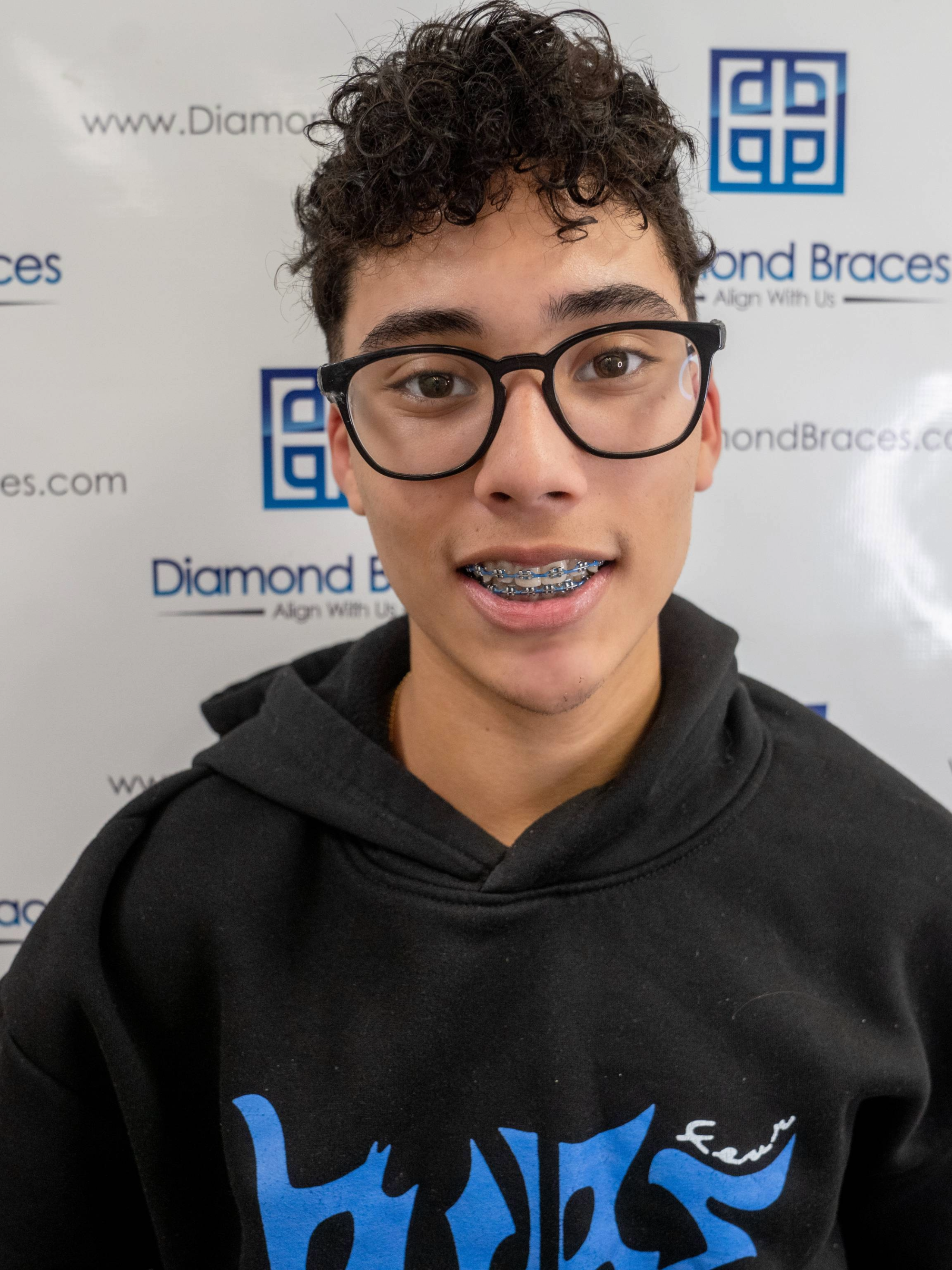 Orthodontic patient wearing a black hoodie with a blue logo in front of a Diamond Braces backdrop.