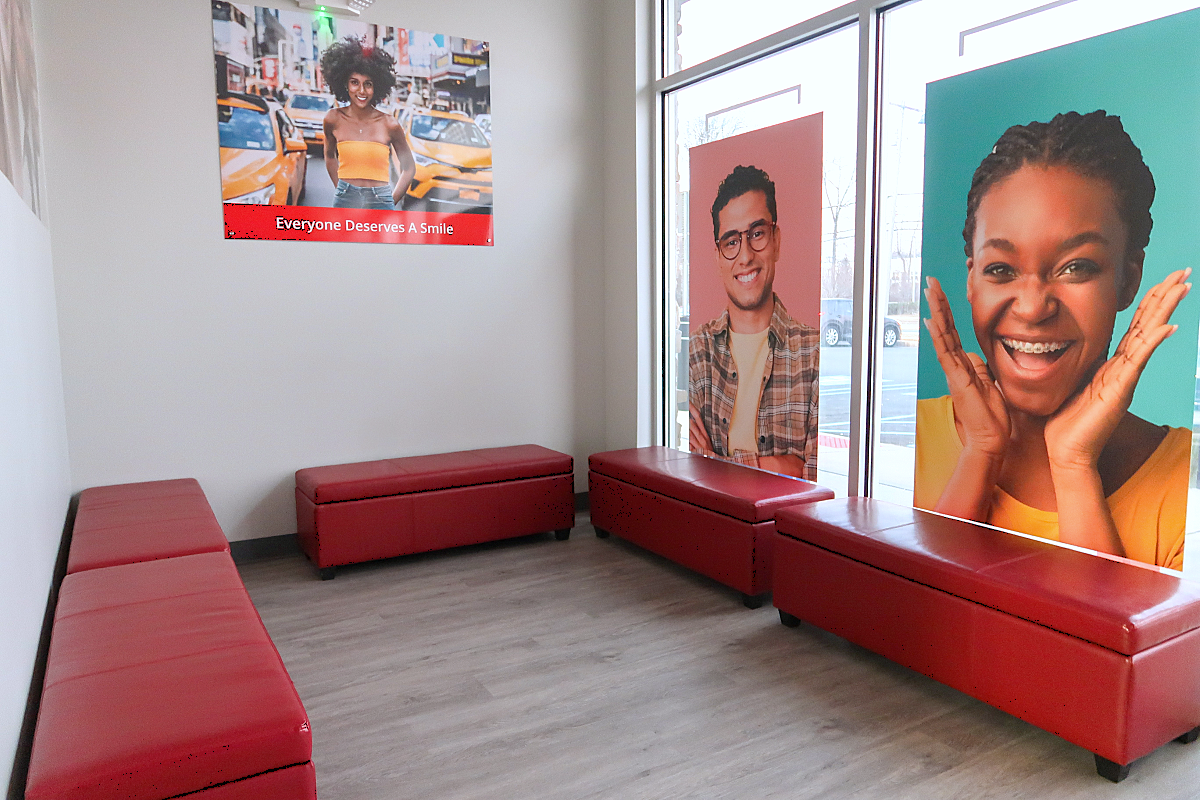 Photo of the Diamond Braces dental office waiting area where there are red rectangle shaped seats, wood paneled flooring and posters of people smiling. 