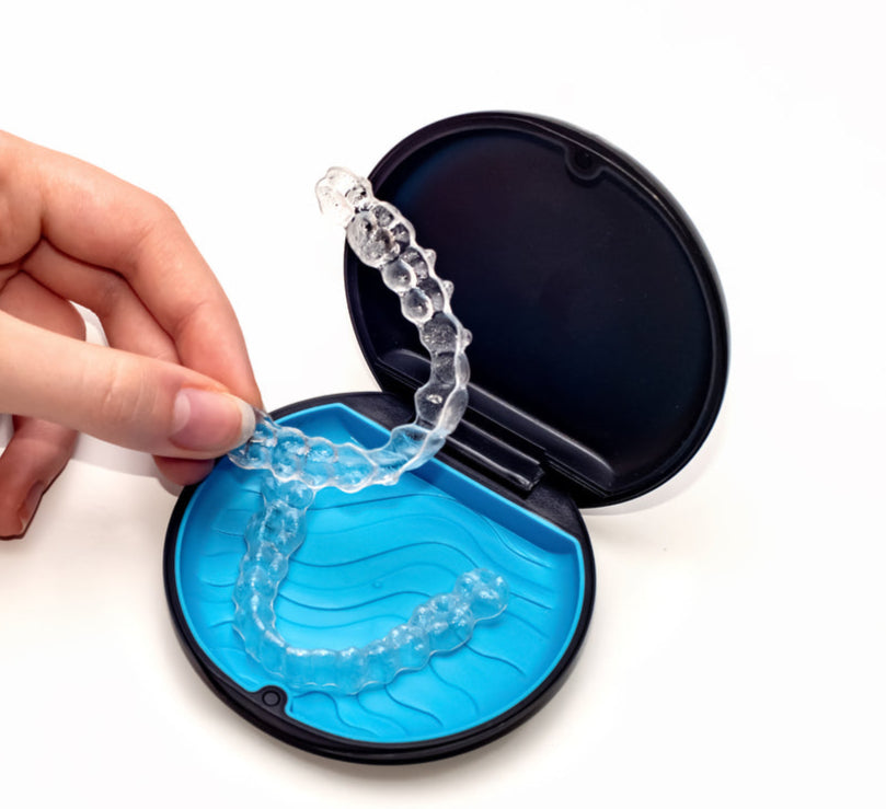 Clear aligner being placed into a blue case by a hand on a white background