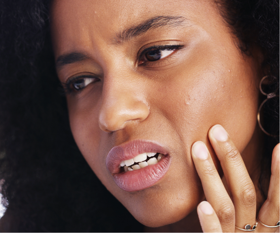 Close-up of a woman with curly hair touching her face.